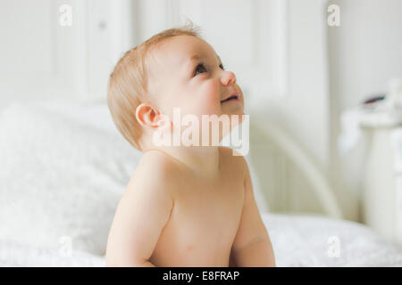 Portrait of Smiling baby sitting on bed in bedroom Stock Photo