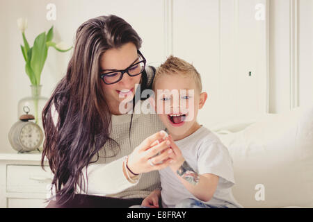 Portrait of a smiling mother and son sitting on bed in bedroom laughing Stock Photo