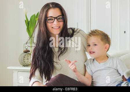 Portrait of a smiling mother and son sitting on bed in bedroom Stock Photo