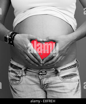 Woman holding heart shape objects in front of her pregnant belly