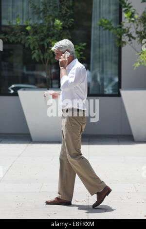 Side view of businessman walking down street while talking on mobile phone Stock Photo