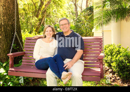 Mature couple sitting on wooden swing in garden Stock Photo
