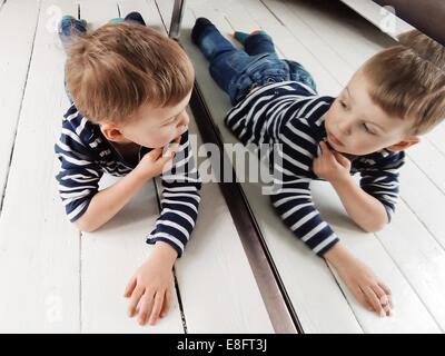 Portrait of a Boy lying on the floor looking at himself in the mirror Stock Photo