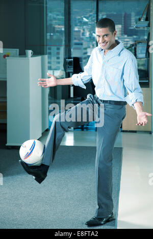 Smiling businessman in office doing kick-ups with football Stock Photo