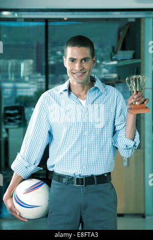 Portrait of smiling Businessman in office holding soccer ball and trophy Stock Photo