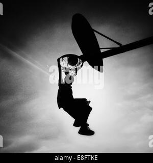 Silhouette of boy playing basketball scoring slam dunk Stock Photo