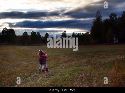 Two girls standing in a meadow hugging each other, Sweden Stock Photo