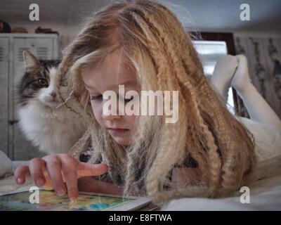 Girl lying on bed with her cat using a digital tablet, Sweden Stock Photo