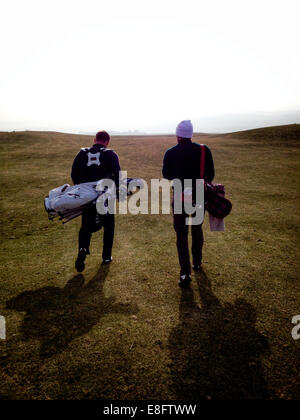 Rear view of two golfers walking on a golf course, Scotland, UK Stock Photo