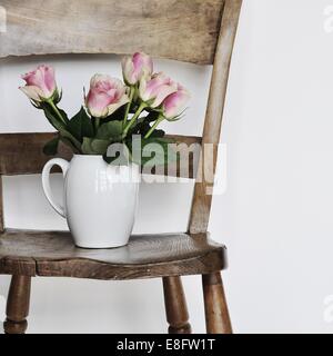 Vase of pink roses on wooden chair Stock Photo