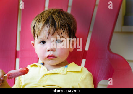 Portrait of a boy with an ice lolly sitting in a chair Stock Photo