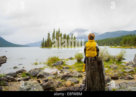 Boy sitting on a tree trunk by a lake, USA Stock Photo