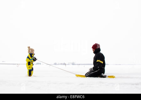 Son pulling father on sledge (2-3 years) Stock Photo