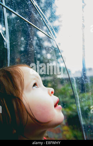 Girl standing in the rain looking through a transparent umbrella, USA Stock Photo