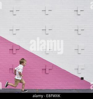 Boy running past pink and white wall Stock Photo