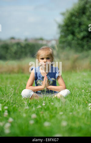 Girl (2-3) sitting on the grass doing yoga Stock Photo
