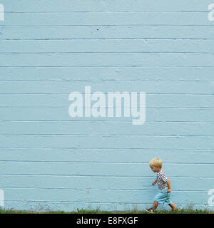 Boy walking past a blue wall Stock Photo