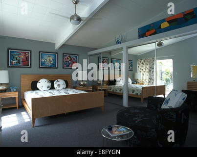 Mirrored doors on fitted wardrobes in modern bedroom with pale wood bed and dark gray sofa Stock Photo