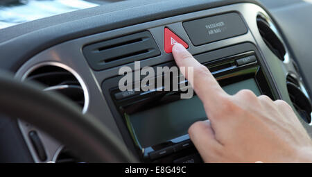 Hand press the emergency warning lights button on the dashboard of a car. Stock Photo