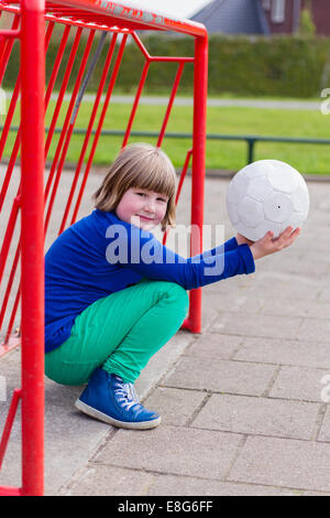 Young crouching girl with ball on hands in metal goal Stock Photo