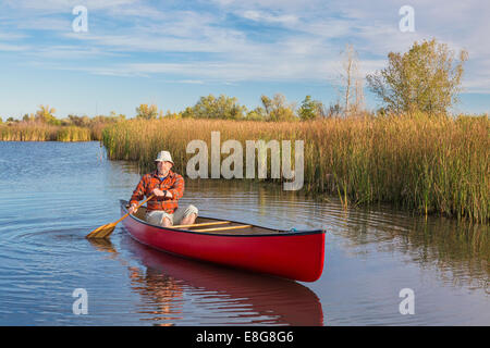 senior male paddler paddling a red canoe on a calm lake, Riverbend Ponds Natural Area, Fort Collins, Colorado Stock Photo