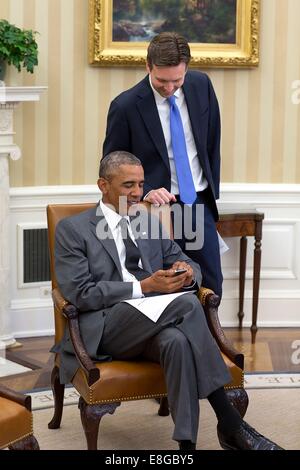 US President Barack Obama looks at photos of Press Secretary Josh Earnest's newborn baby boy, Walker, during a meeting with senior advisers in the Oval Office of the White House August 25, 2014 in Washington, DC. Stock Photo