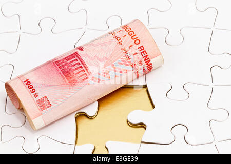 Chinese yuan on puzzle with missing piece. Business concept of finance shown with currency and gold beneath. Stock Photo
