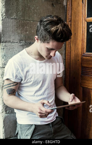 Young man using digital tablet while leaning on high school wall Stock Photo