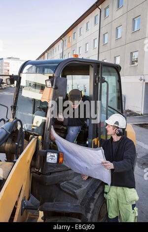 Construction workers discussing over blueprint at excavator Stock Photo