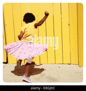 Girl spinning around dancing in front of a yellow wall, San Francisco, California, USA Stock Photo