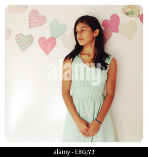 Girl leaning against a wall decorated with hearts looking sideways Stock Photo