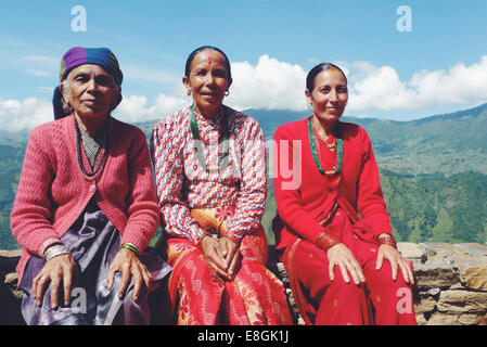 Portrait of three local Nepalese women sitting on a wall in a mountain village, Nepal Stock Photo