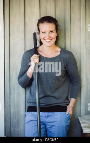 Portrait of happy woman holding shovel while standing against wall Stock Photo