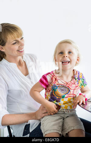 Happy girl sitting on mother's lap at home Stock Photo