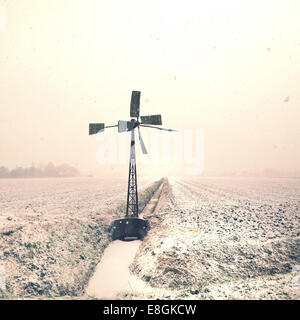 Wind turbine by a levee in the snow, Netherlands Stock Photo