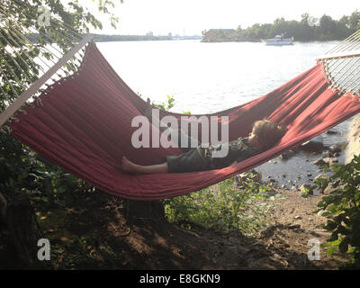Boy lying in a hammock by a lake, Sweden