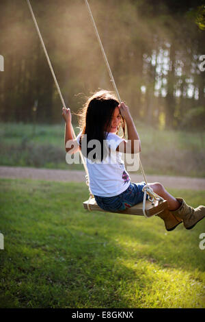 Smiling girl sitting on a rope swing in the garden, Mississippi, USA Stock Photo