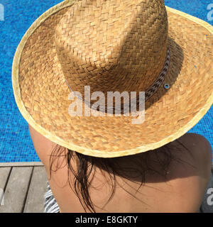 Woman in sun hat sitting by swimming pool Stock Photo