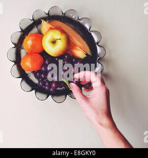 Woman's hand reaching for grapes in fruit bowl Stock Photo