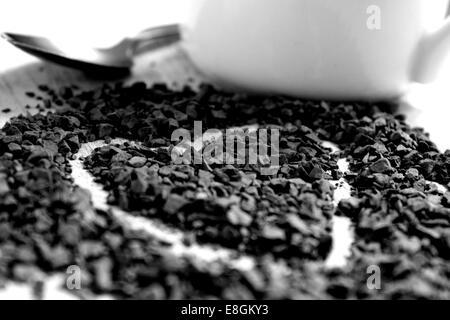 A heart drawn in coffee granules alongside a small silver spoon and white mug Stock Photo