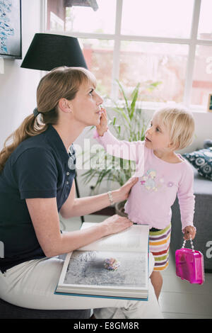 Girl putting make-up on mother at home Stock Photo