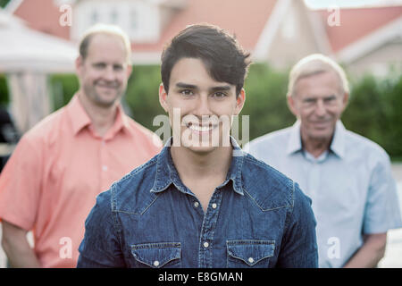 Portrait of confident young man with grandfather and father standing in yard Stock Photo