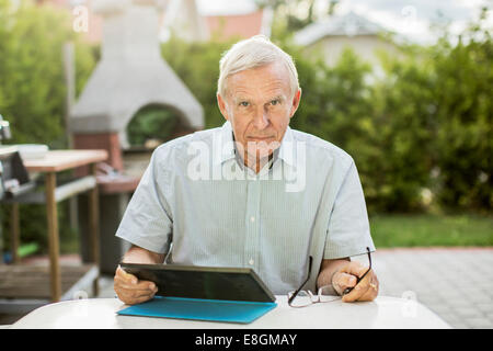 Portrait of confident senior man using digital tablet at table in yard Stock Photo