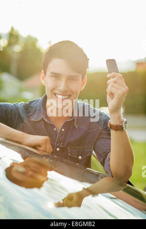 Portrait of happy young man showing key while leaning on car Stock Photo