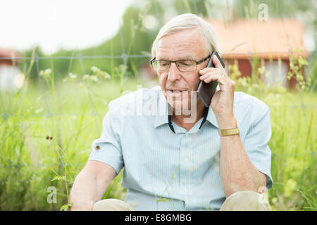 Senior man using mobile phone while sitting in yard Stock Photo