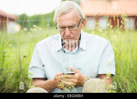 Senior man text messaging on mobile phone while sitting in yard Stock Photo