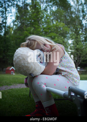 Sweden, Girl (6-7) hugging teddy bear in backyard Stock Photo