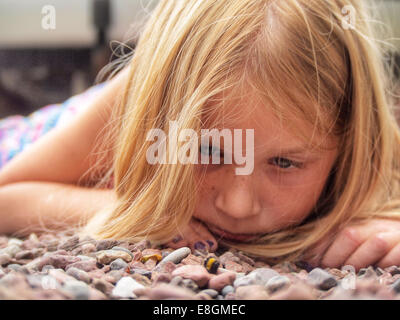 Girl lying on the ground outdoors looking at a dead bumblebee, Sweden Stock Photo