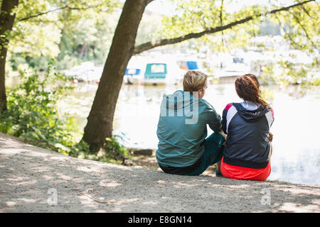 Rear view of fit couple relaxing at lakeshore Stock Photo