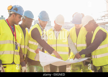 Architect explaining plan on blueprint to construction workers at site Stock Photo